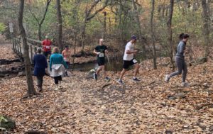 Several runners and walkers are moving through a wooded trail in Watham, MA