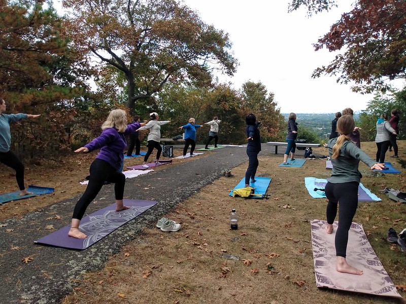 People do yoga outside with Boston skyline on the horizon.